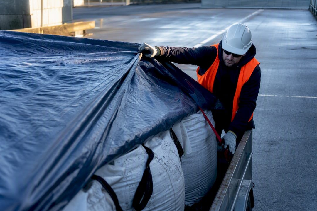 Worker securing covered asbestos soil load